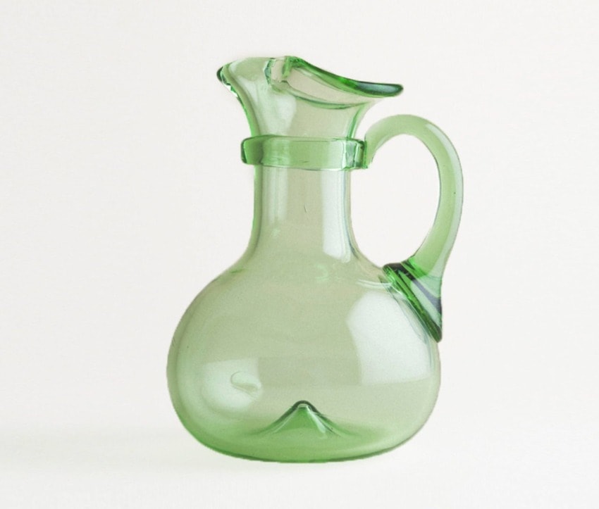 Green glass pitcher with a curved handle and wide base against a plain white background.