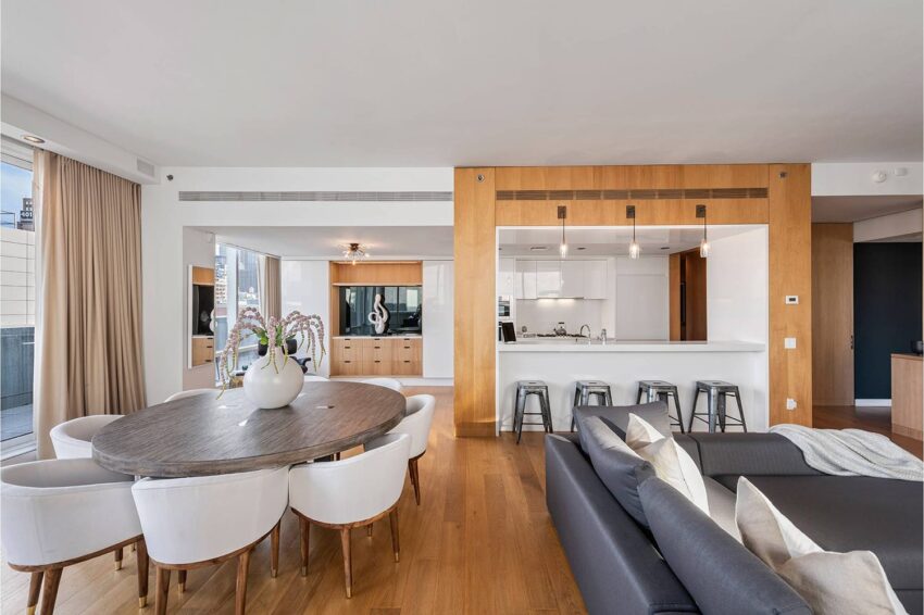 Modern open-plan living room and kitchen with wooden floors, a round dining table, and a gray sofa.