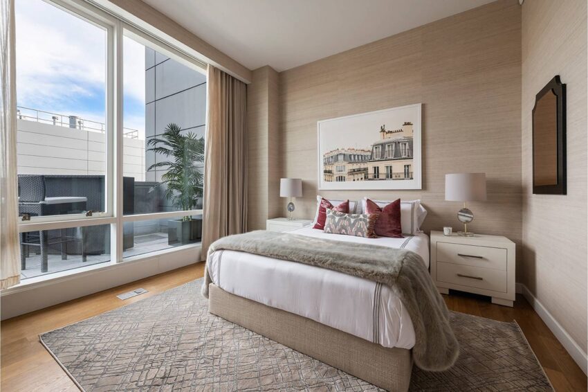 Modern bedroom with large window, double bed, decorative pillows, rug, and artwork on the wall.