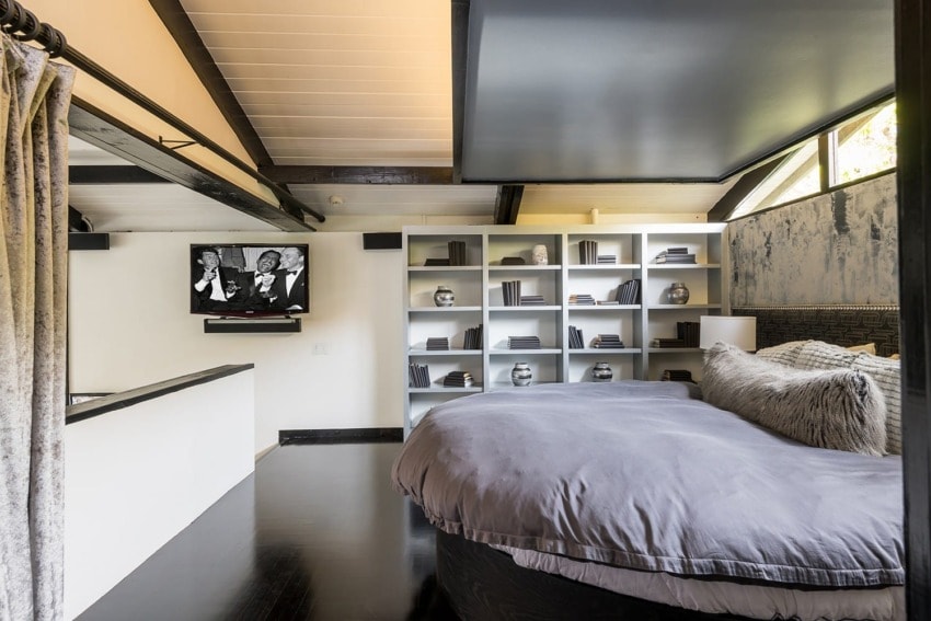 Modern bedroom with circular bed, wall-mounted TV, and minimalist bookshelf in a stylish, open-concept design.