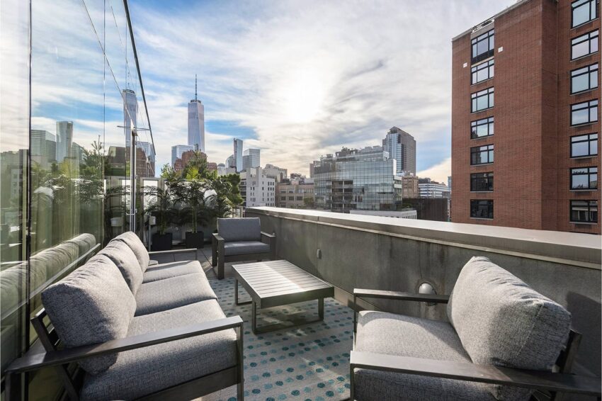 Rooftop patio with modern seating and city skyline view in the background under a partly cloudy sky.