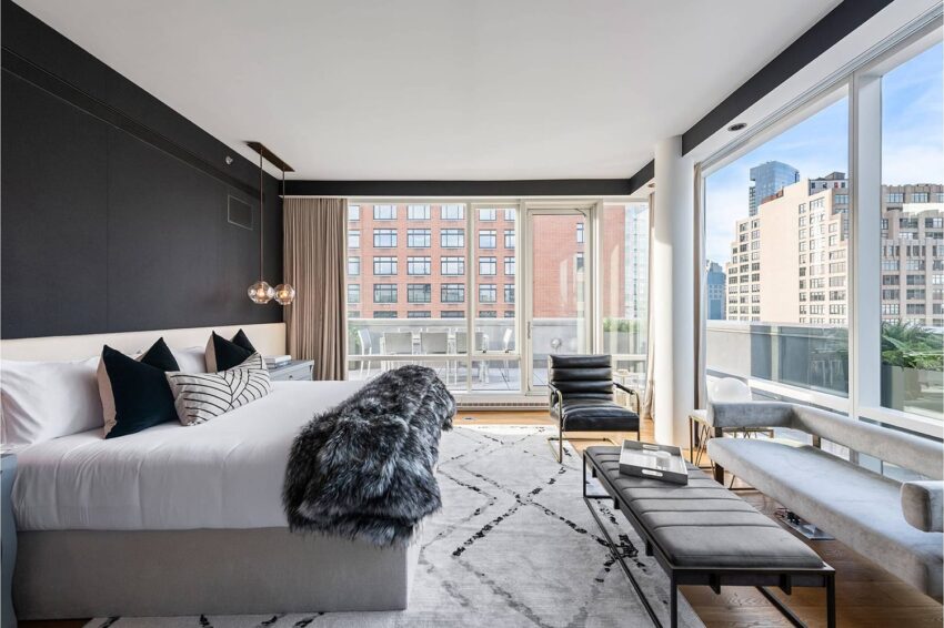 Modern bedroom with large windows, city view, cozy bedding, and stylish furniture, featuring a black and white color scheme.