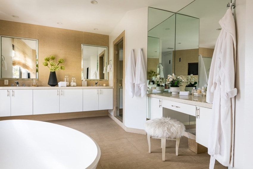 Modern bathroom with large mirrors, white cabinets, fluffy stool, and greenery accents for a fresh, elegant feel.