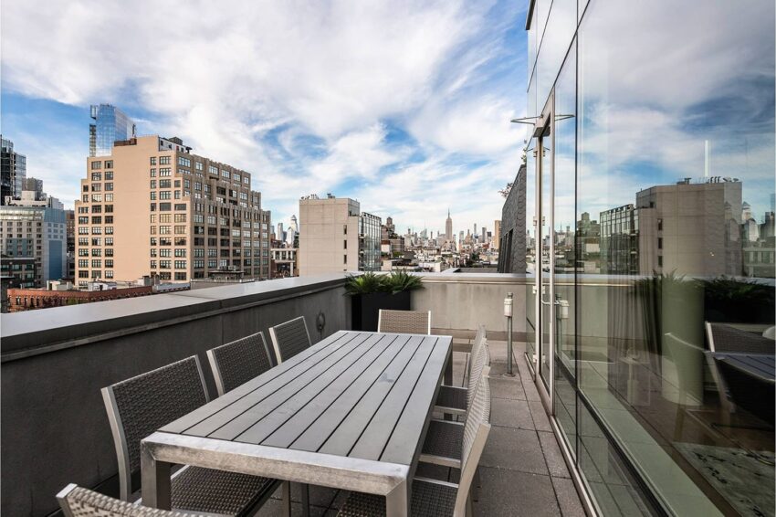 Rooftop patio with a dining table overlooking a city skyline under a partly cloudy sky.