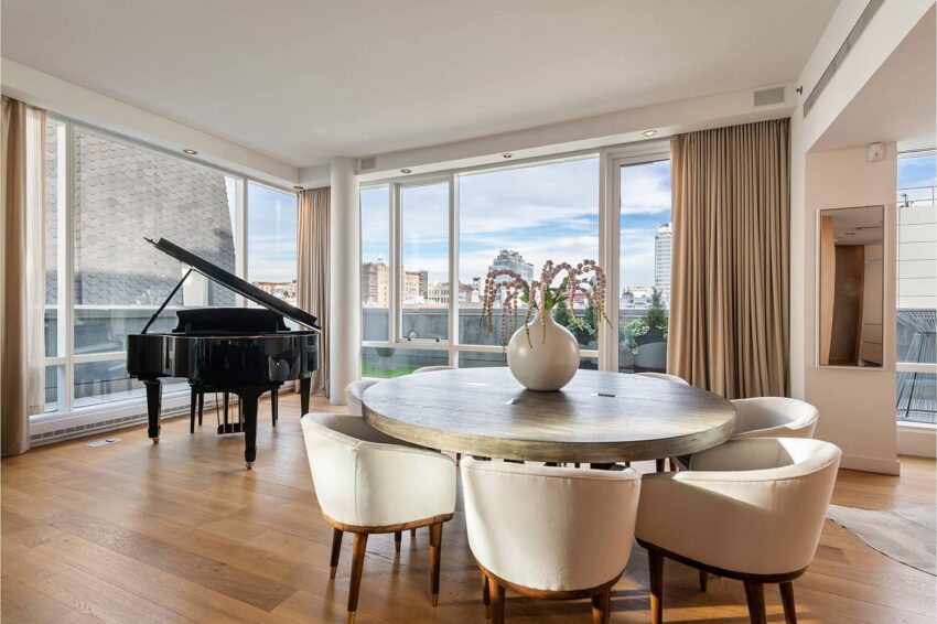 sunlit modern dining area with round table white chairs grand piano and city view through large windows