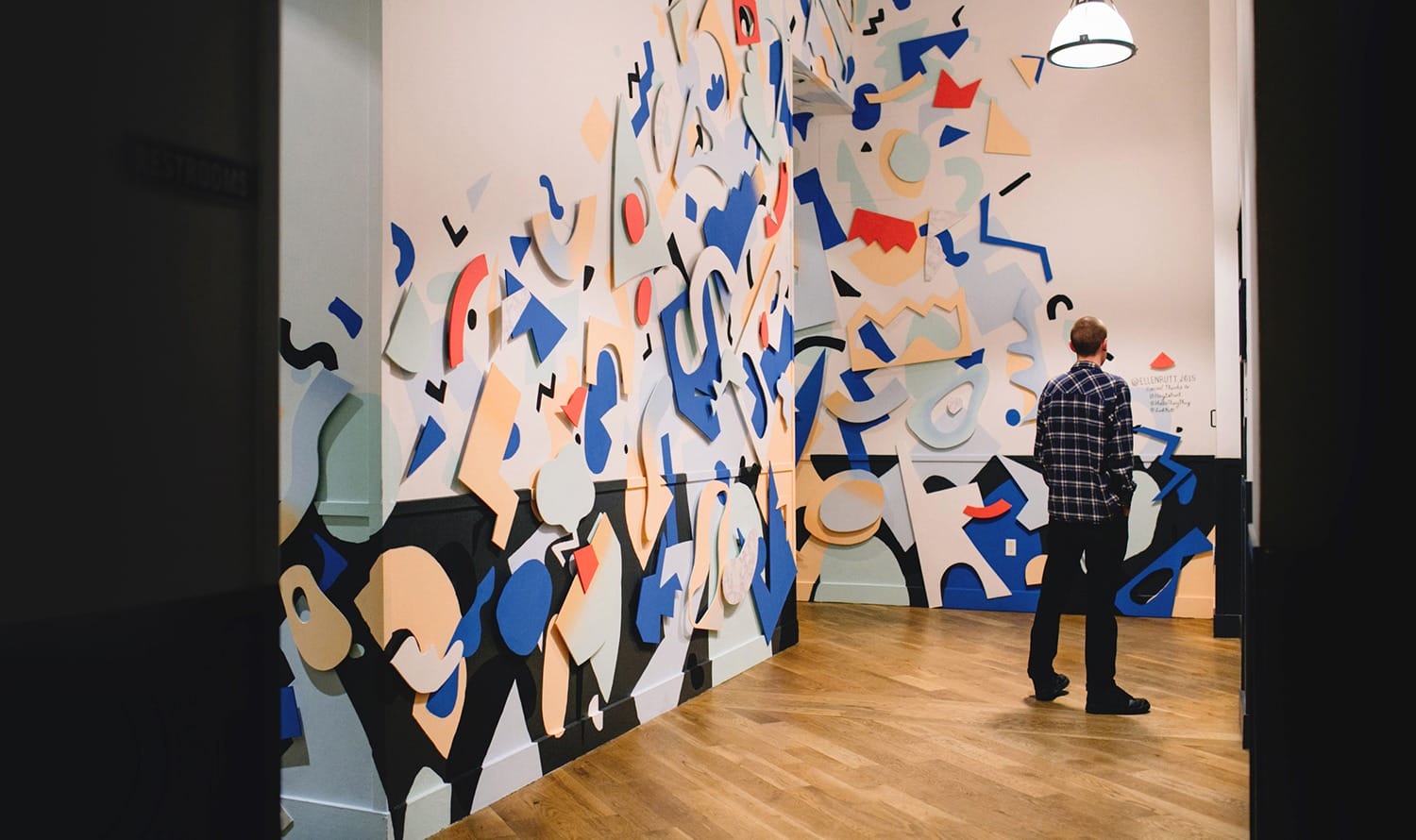 Man admiring colorful abstract mural on indoor wall with wooden flooring and overhead lighting