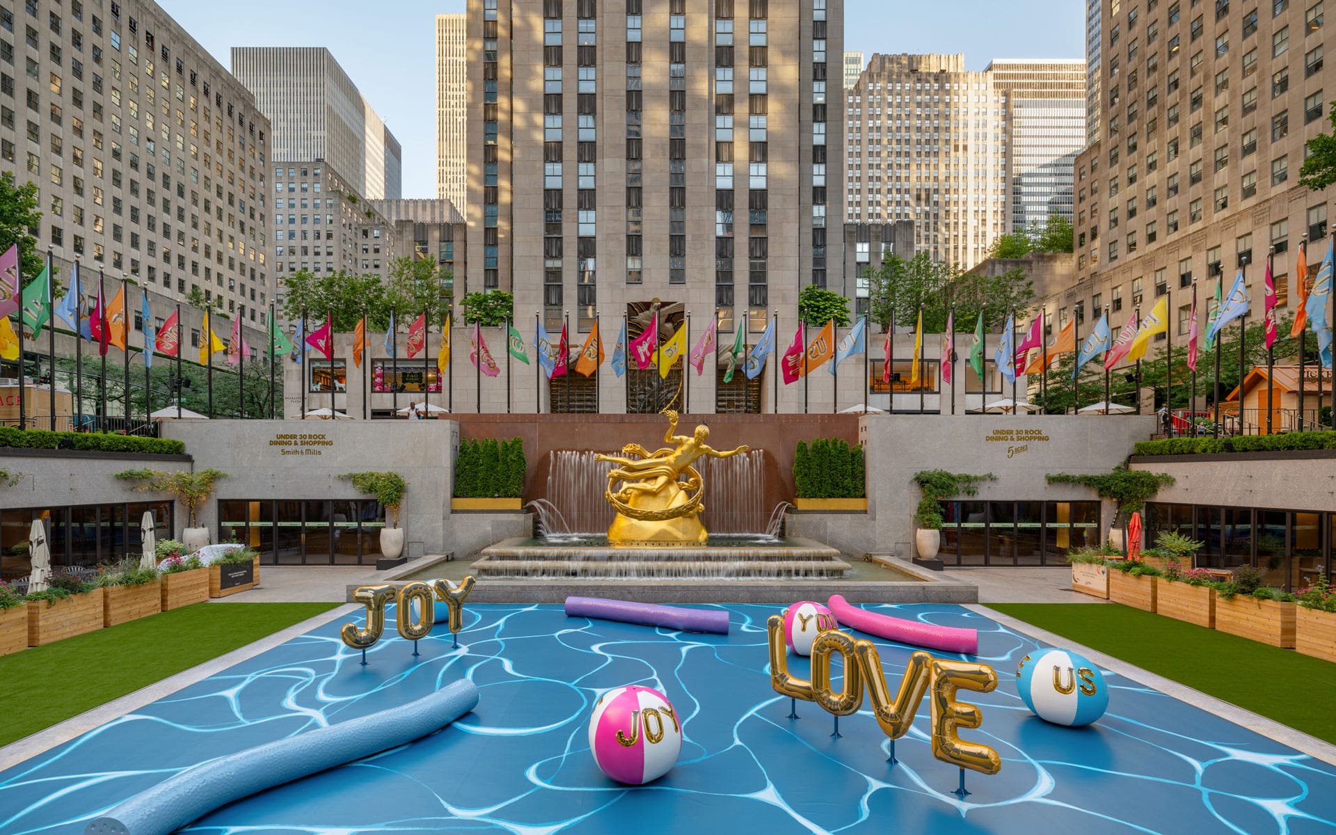 Rockefeller Center plaza with pool float decorations, colorful flags, and Prometheus statue in New York City.