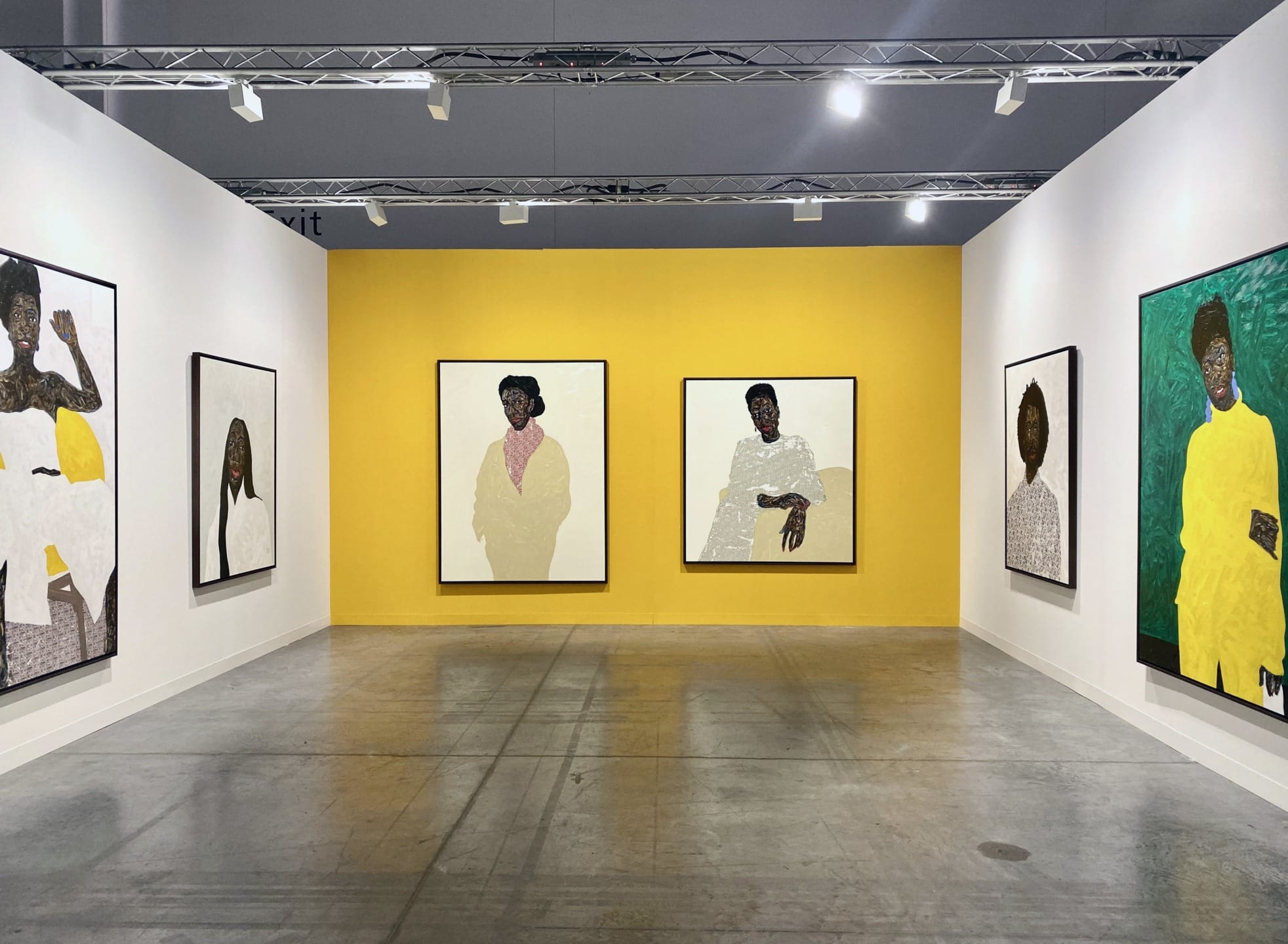 Art gallery with six large framed portraits on yellow and white walls, displayed under bright lighting.
