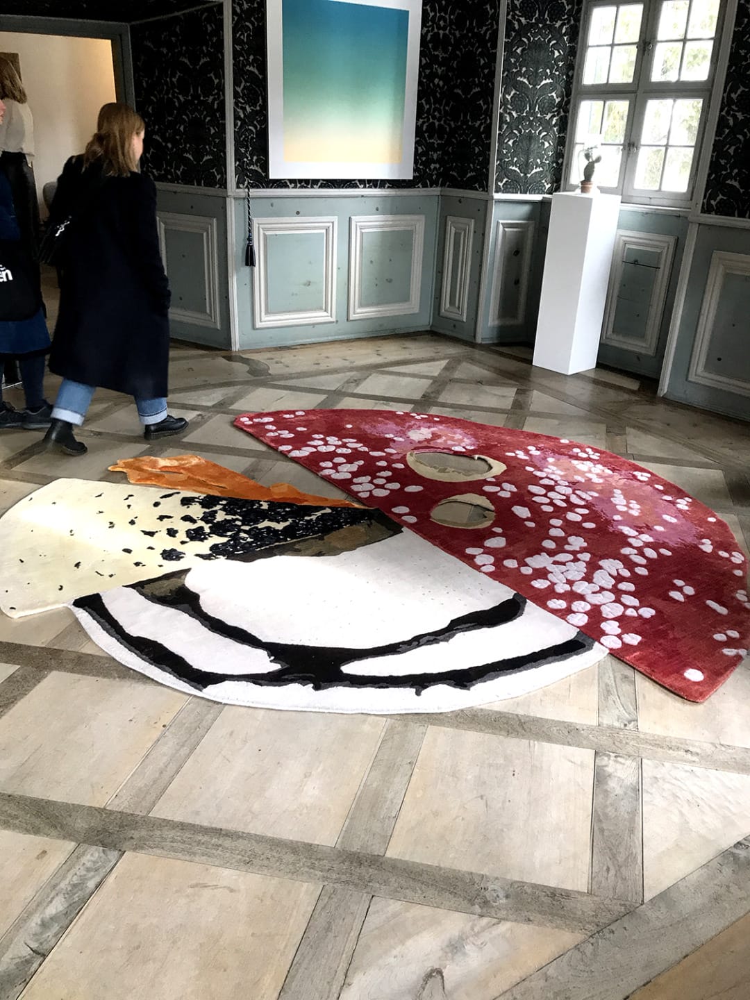 Art installation on a wooden floor depicting a split mushroom motif with visitors observing in a gallery setting.