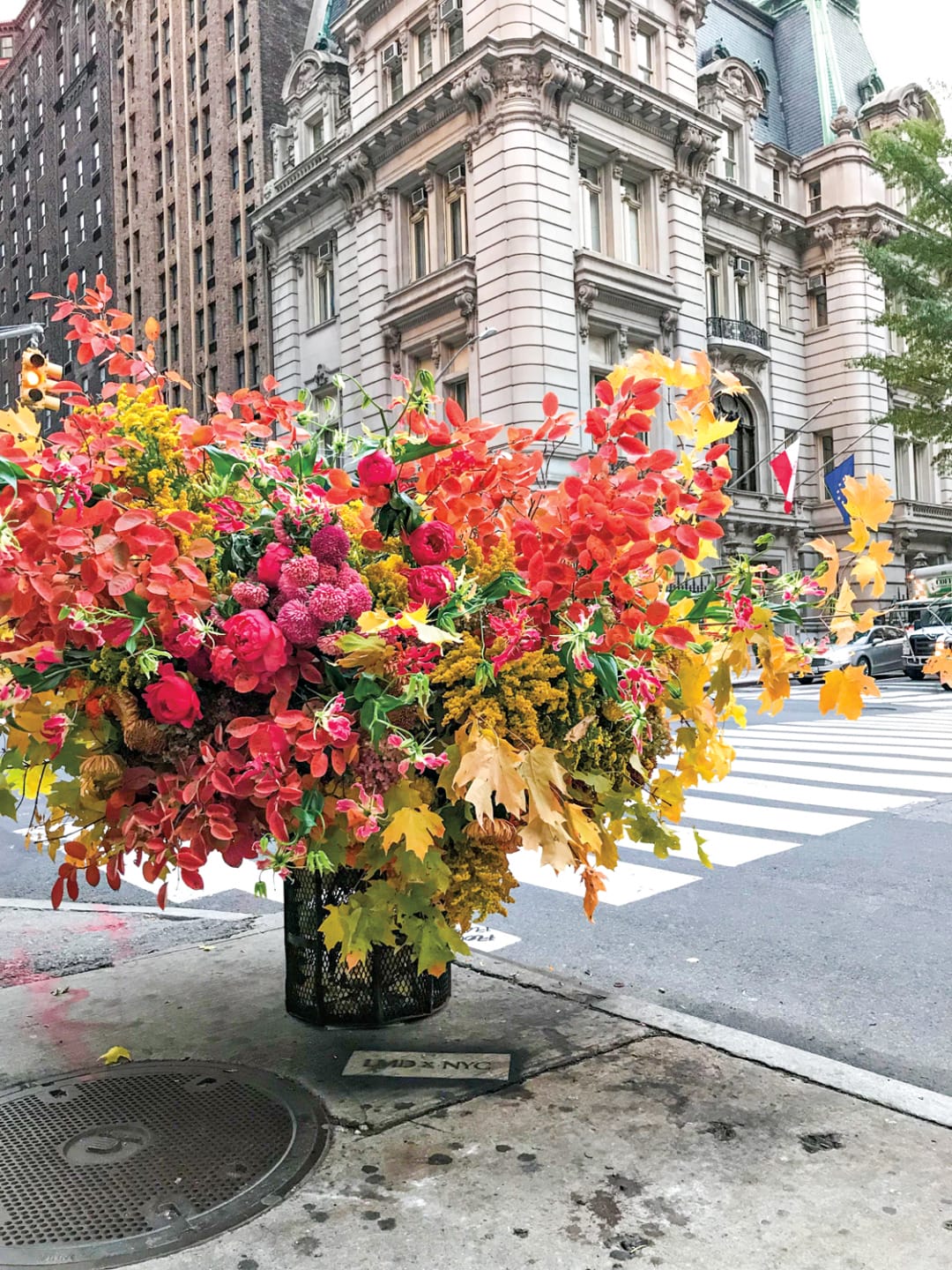 Vibrant autumn floral arrangement on a city sidewalk with historic building and crosswalk in the background.