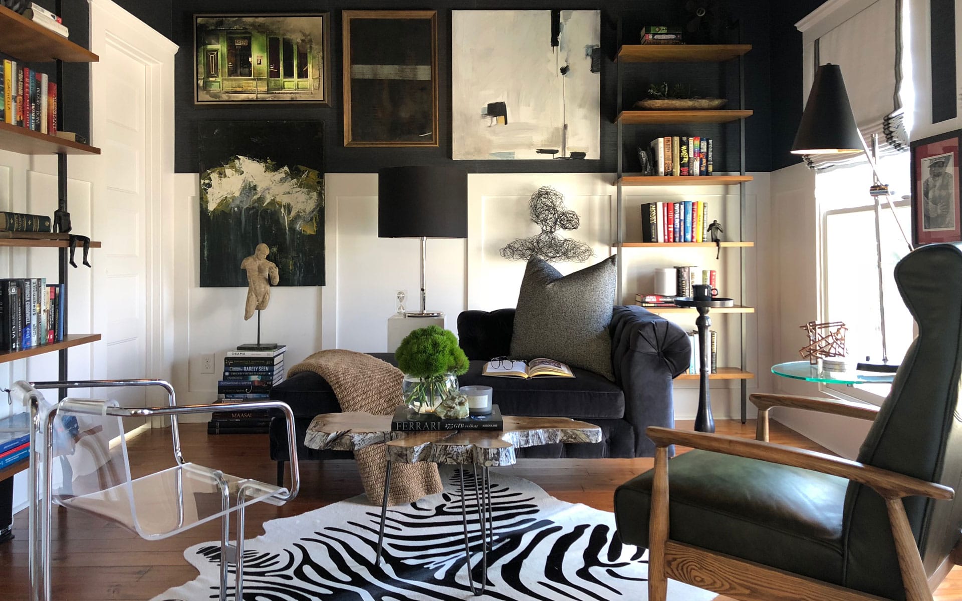Cozy living room with eclectic decor, bookshelves, a zebra-print rug, and modern art on dark walls.