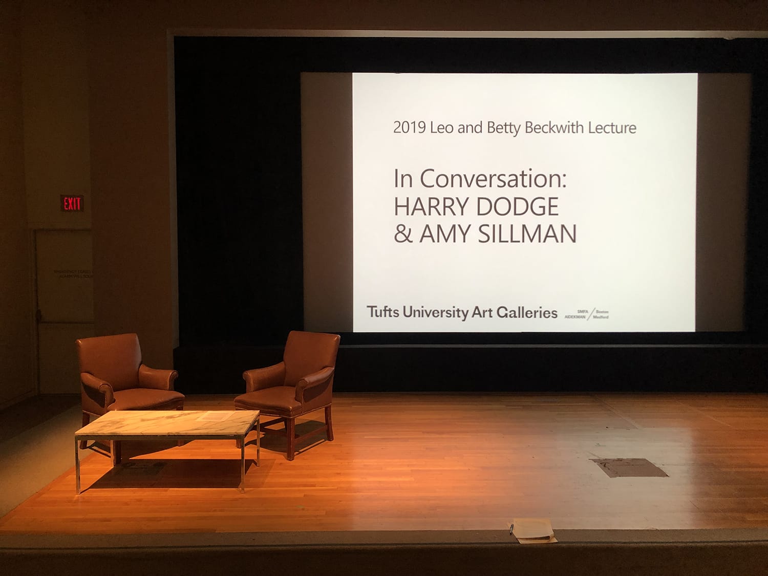Stage with two chairs and presentation screen promoting 2019 Leo and Betty Beckwith Lecture featuring Harry Dodge and Amy Sillman.
