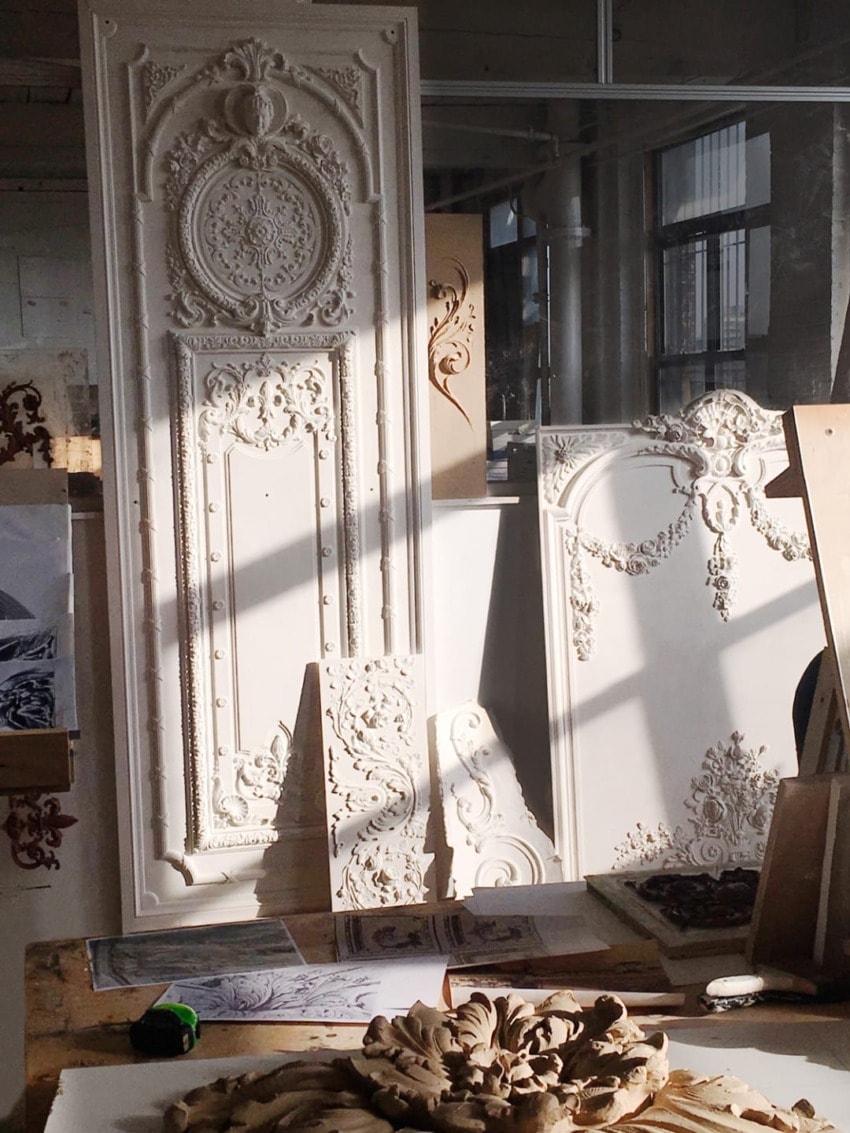 Elegant white architectural plaster molds and reliefs on display in a sunlit workshop setting.