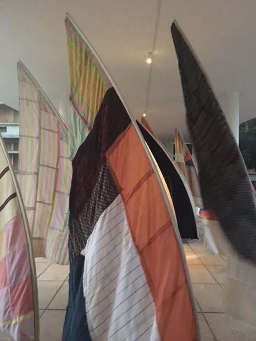 Colorful patchwork sails displayed indoors on curved frames, creating an artistic installation with soft lighting.