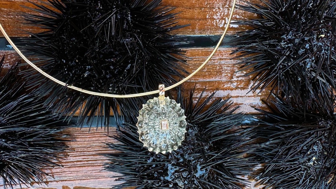 Gold necklace with spiky pendant resting on black sea urchins against a wooden background.