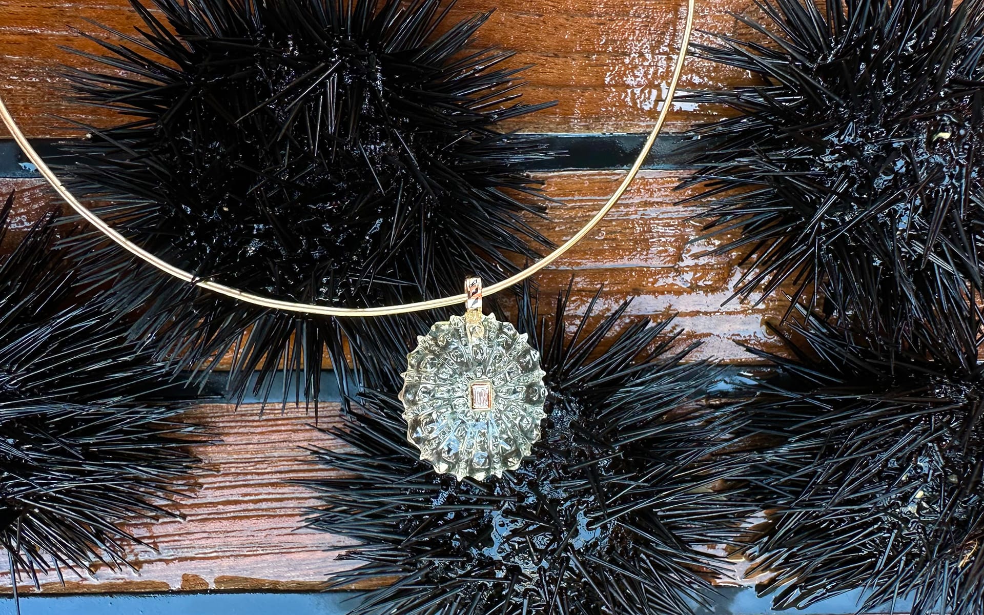 Gold necklace with spiky pendant resting on black sea urchins against a wooden background.