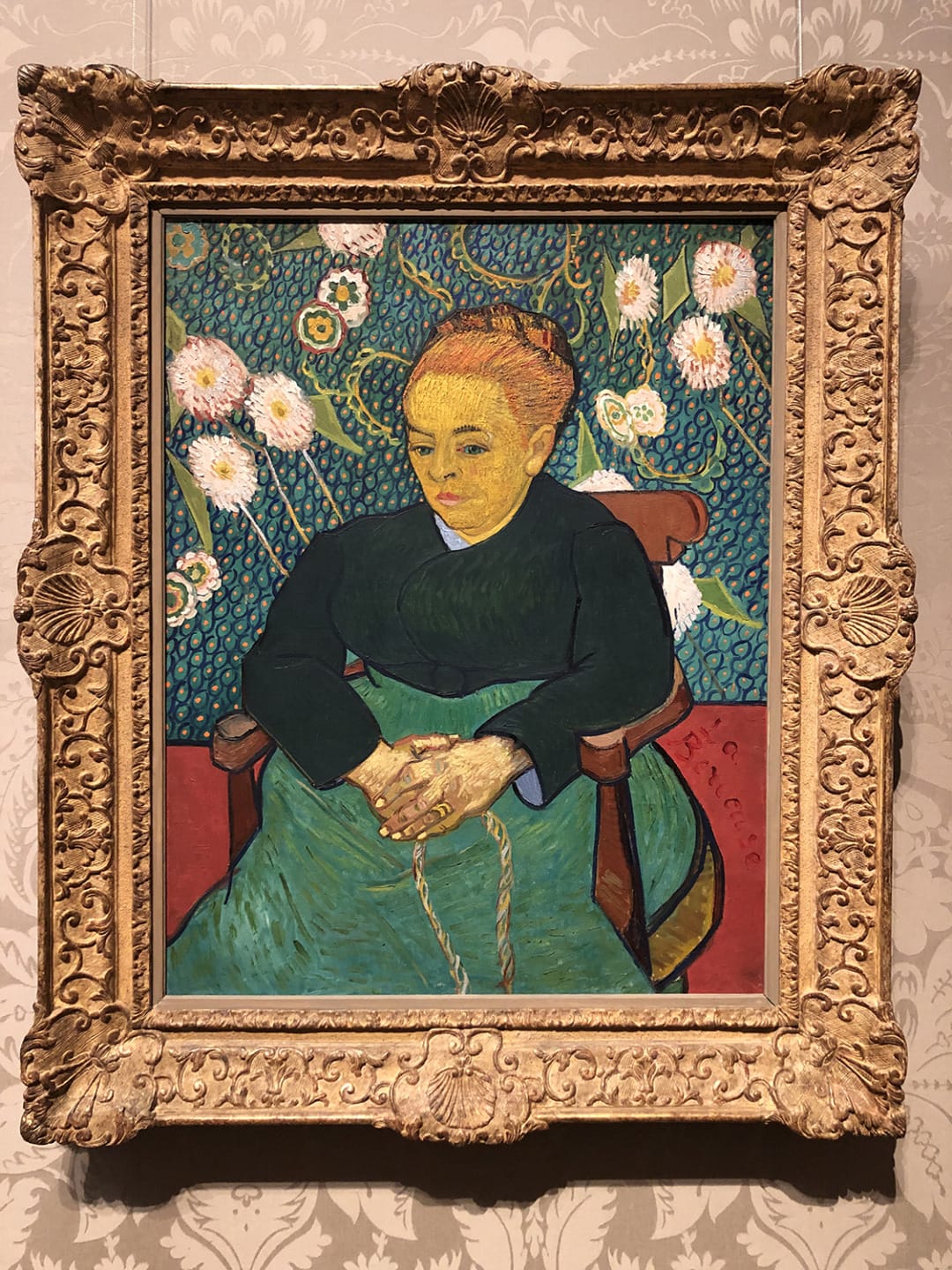 Painting of a woman with red hair seated in front of white flowers, framed with an ornate gilded border.