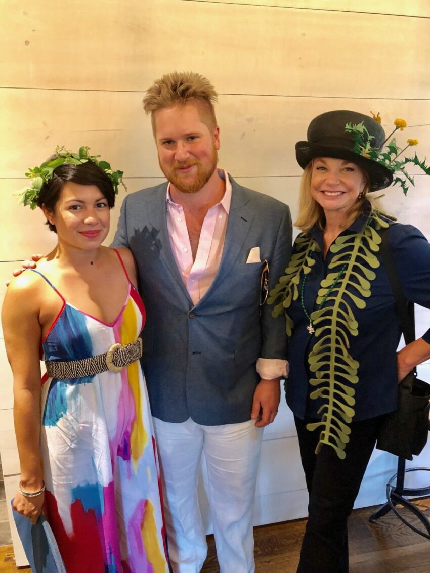 Three people dressed in colorful and festive attire, one wearing a floral crown and another a hat with greenery.
