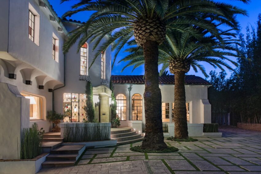 Elegant house with tall palm trees in front, lit up at dusk, featuring multiple windows and a tiled roof.