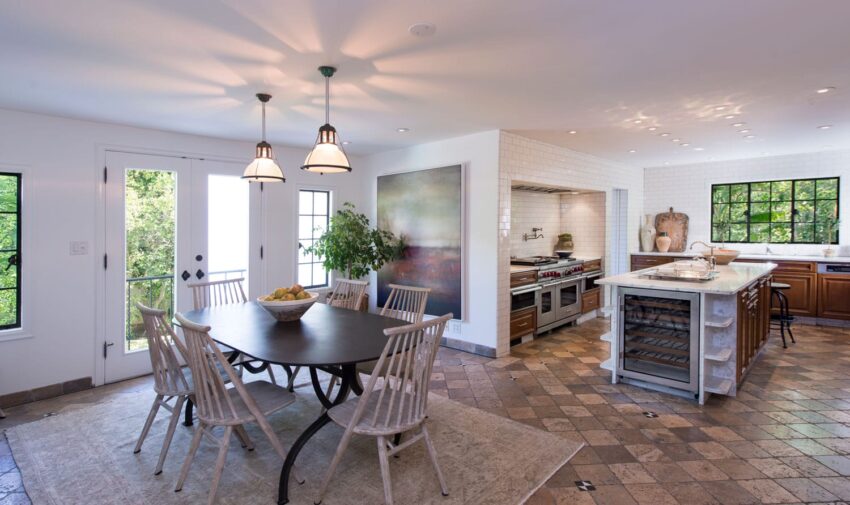 Spacious kitchen and dining area with modern decor, featuring a round table, chairs, and large windows overlooking greenery.