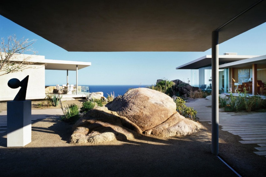 Modern architectural design with geometric structures, large rock centerpiece, and ocean view in the background.