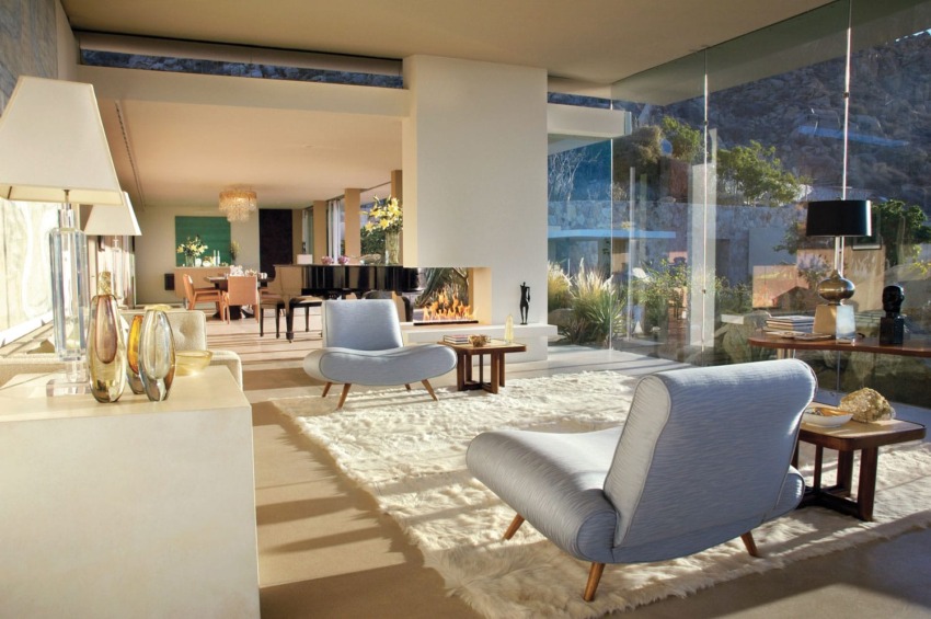 Modern living room with plush chairs, large windows, shag rug, and a view of a scenic outdoor landscape.