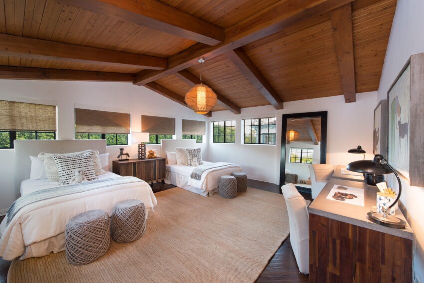 Spacious bedroom with two beds, wooden ceiling beams, large windows, and a desk in a modern rustic style.