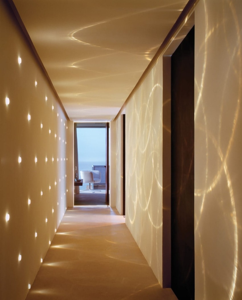 Modern hallway with illuminated circular patterns on walls leading to a room with a view of the ocean through a large window.