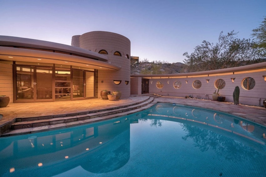 Curved modern house with circular windows and a pool at sunset, surrounded by desert landscaping.