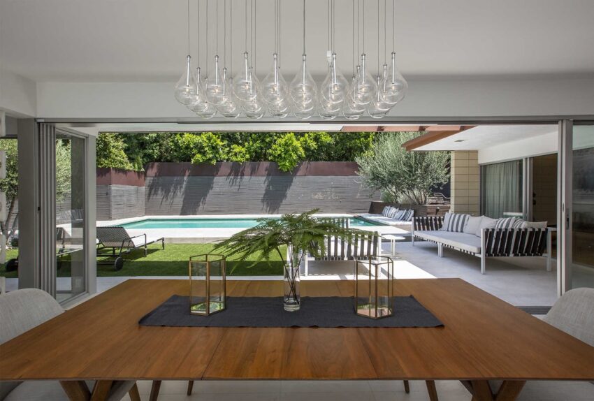 Modern dining room with wooden table, elegant light fixture, and a view of a pool and patio through large sliding doors.