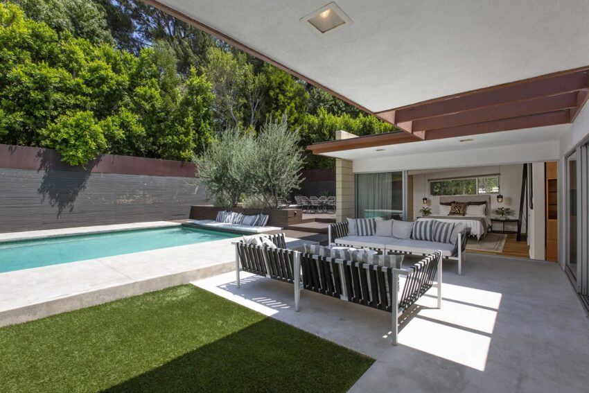 Modern patio with striped furniture, a pool, and trees in the background under a clear sky.