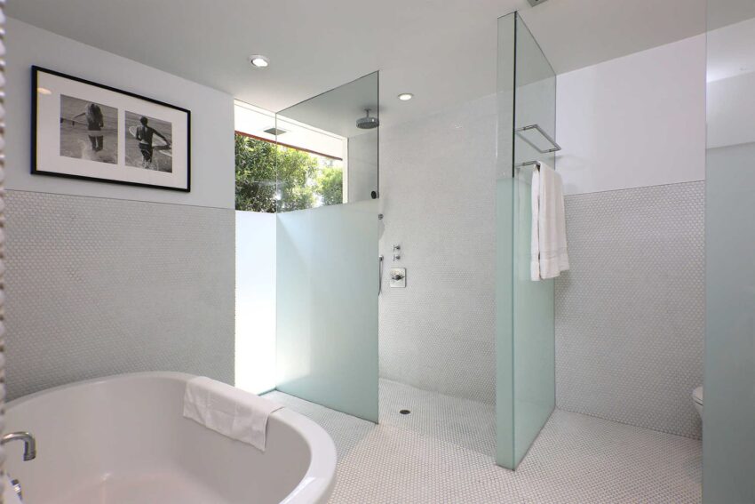 Modern bathroom with glass shower, white tub, towel, and framed artwork on the wall. Minimalist design with natural lighting.