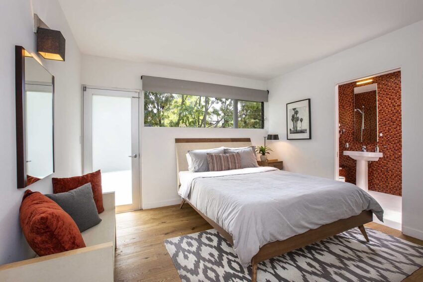Modern bedroom with a large bed, patterned rug, and view into a bathroom with stylish orange tiles.