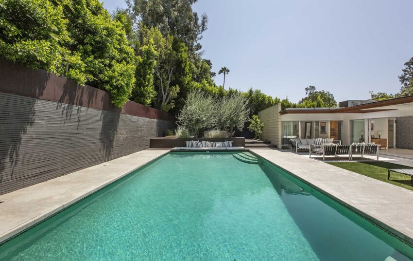 Modern backyard with clear swimming pool, surrounded by trees and outdoor seating, adjacent to a contemporary house.