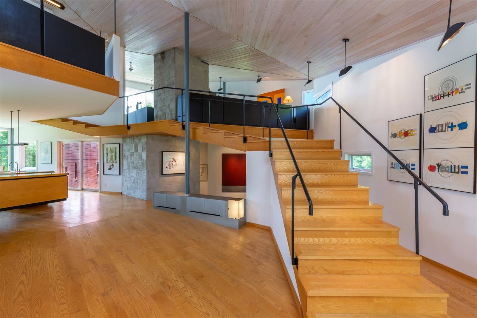 Modern interior with wooden staircase, open layout, art on walls, and natural light from large windows.