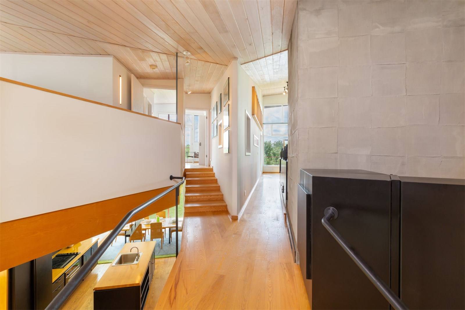 Modern interior hallway with wooden flooring, open staircase, and large windows showcasing a scenic view outside.