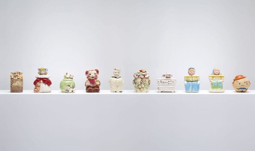 A row of ten vintage cookie jars on a white shelf, each with a unique design and colorful appearance.