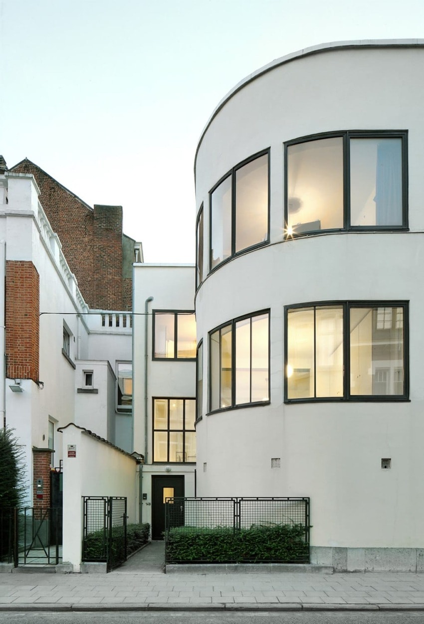Modern white building with large windows, featuring curved lines, set against a clear sky, blending contemporary and classic architecture.