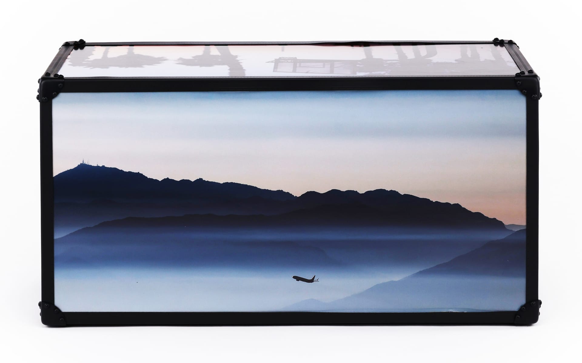 Decorative box with scenic mountain landscape and airplane flying in sky at sunset.