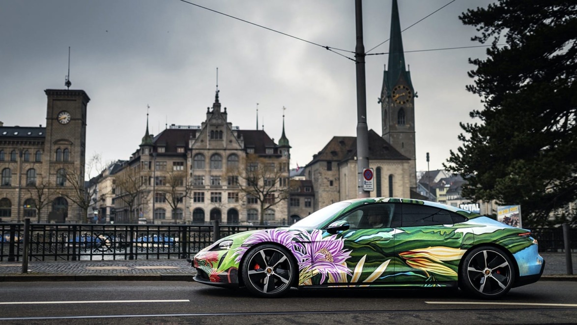 Colorful car with floral wrap parked on a city street with historical buildings and a church in the background.