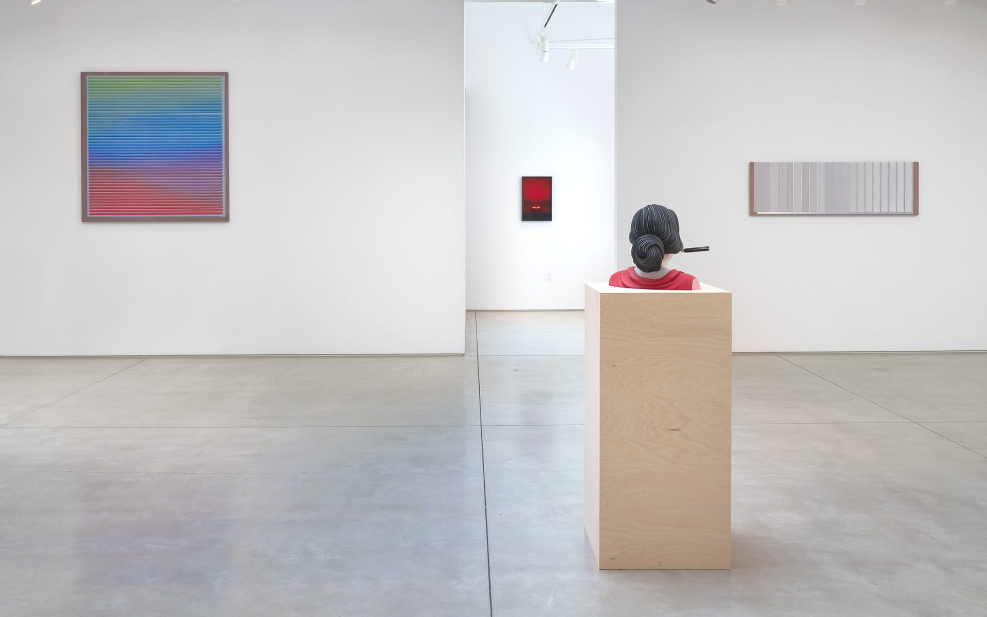 Art gallery with colorful paintings on white walls and a sculpture of a human head on a wooden pedestal in the foreground.