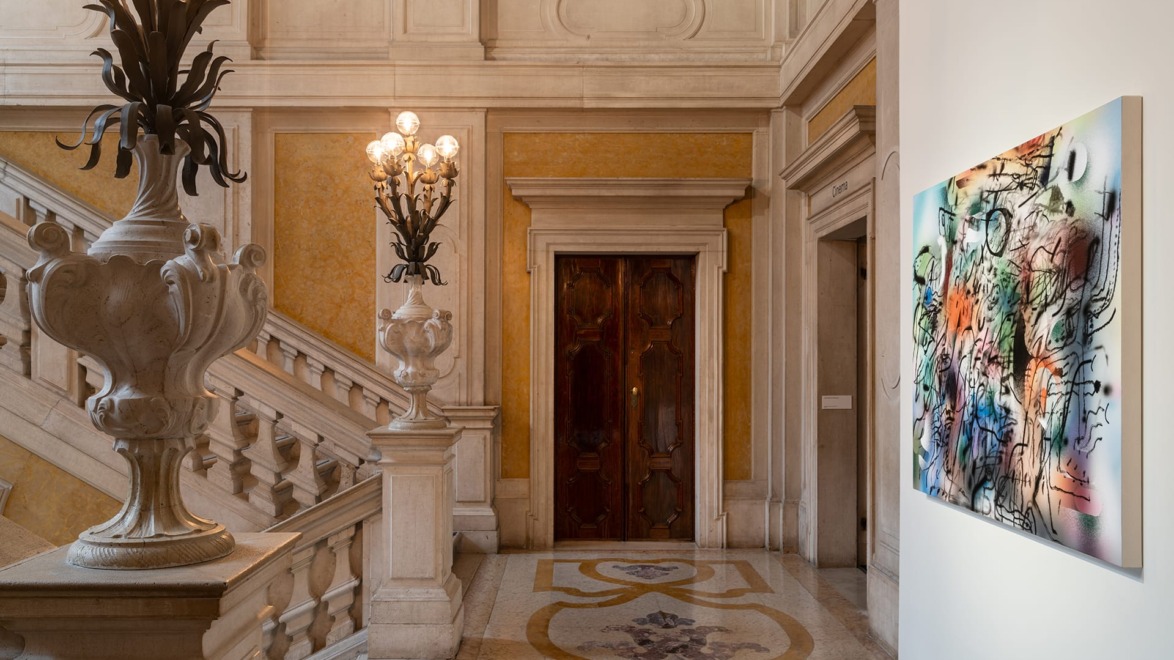 Elegant staircase with ornate railing and decorative wall art in a historic building's corridor.