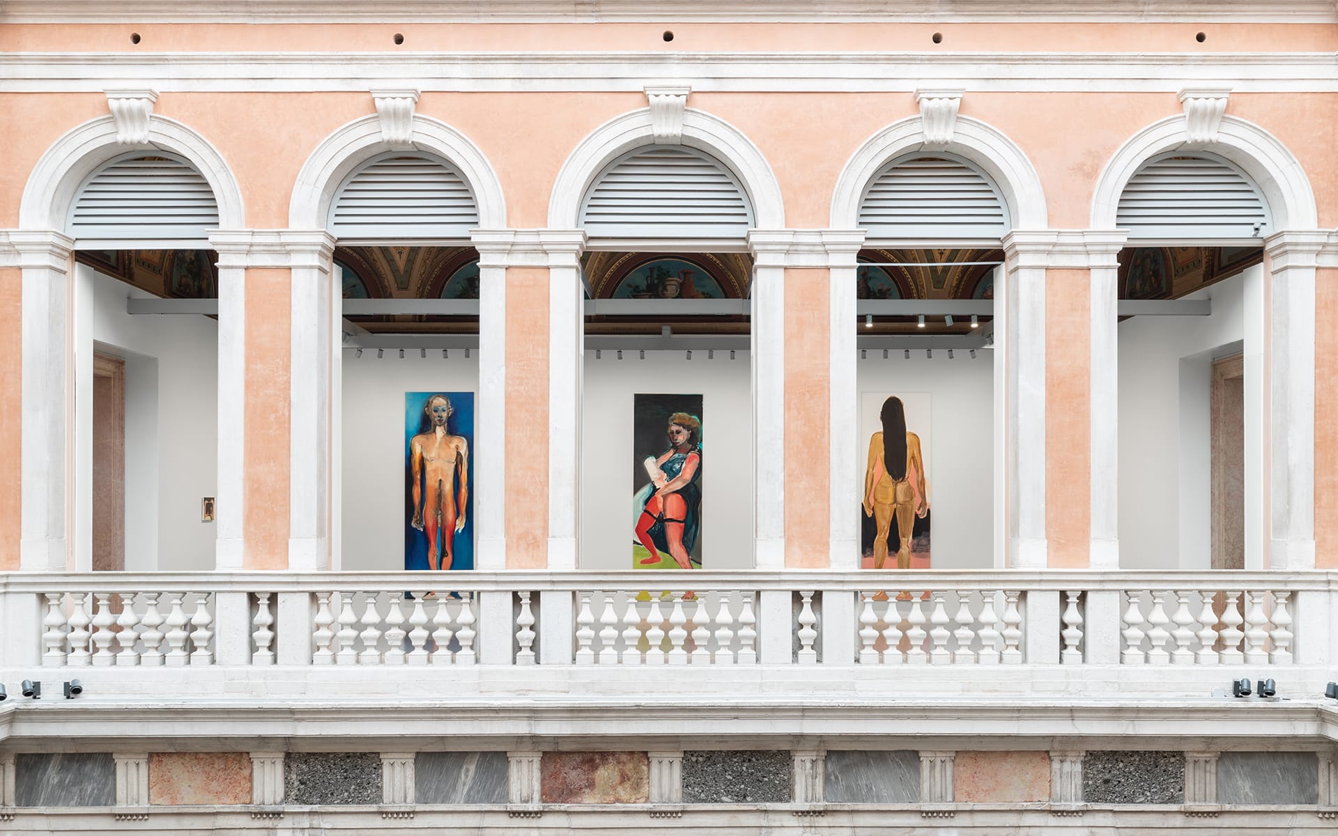 Art exhibition with three large paintings displayed in an elegant building with arches and a white marble balcony.