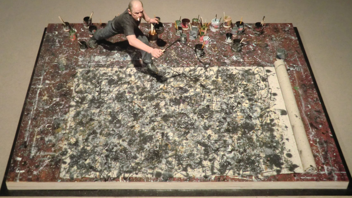 Miniature figure of an artist painting a large abstract canvas with various paint cans surrounding the artwork on the floor.