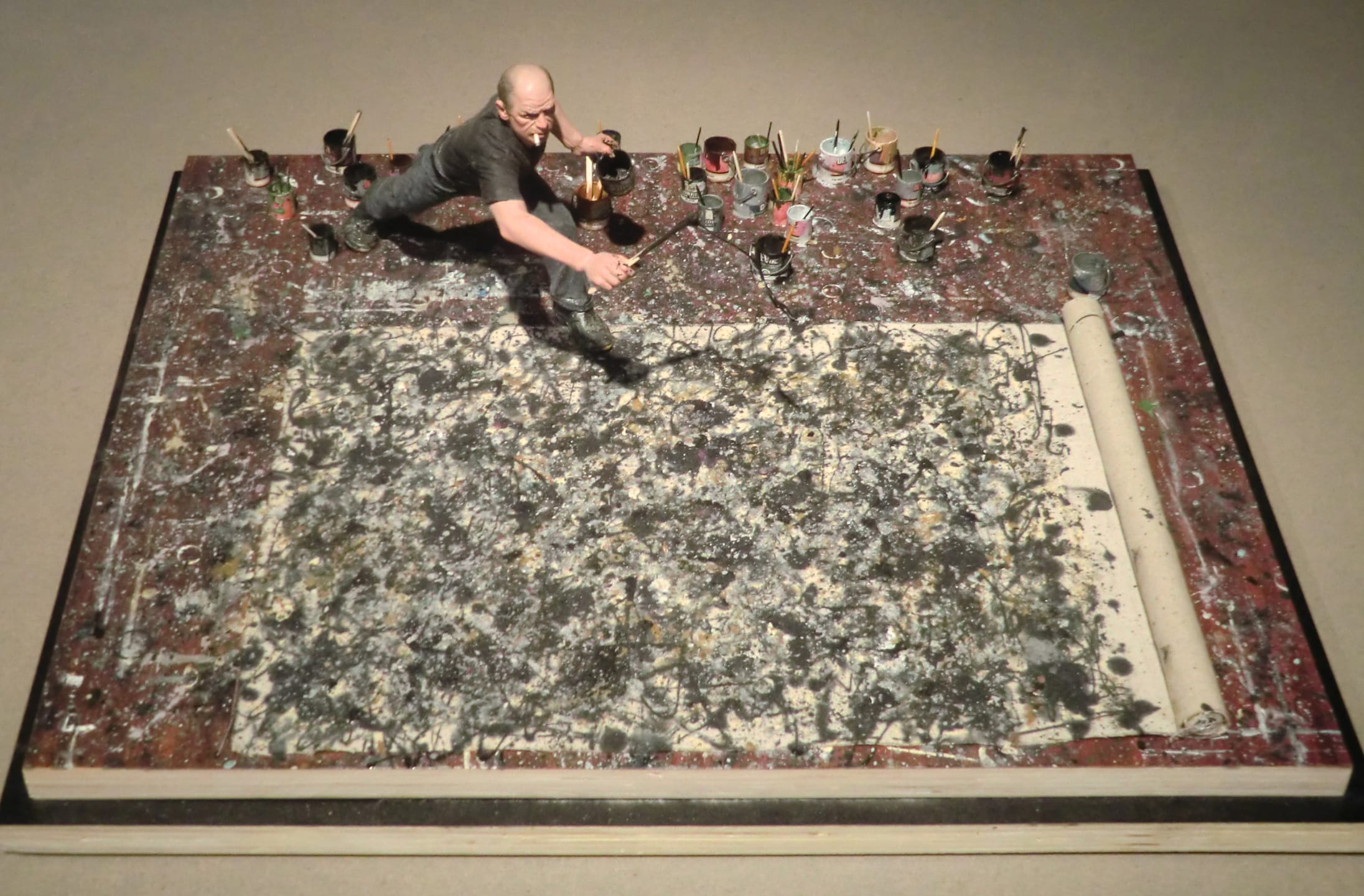 Miniature figure of an artist painting a large abstract canvas with various paint cans surrounding the artwork on the floor.