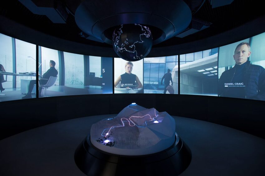 Interactive exhibit featuring screens with various people, a glowing central globe, and a model landscape with illuminated paths.