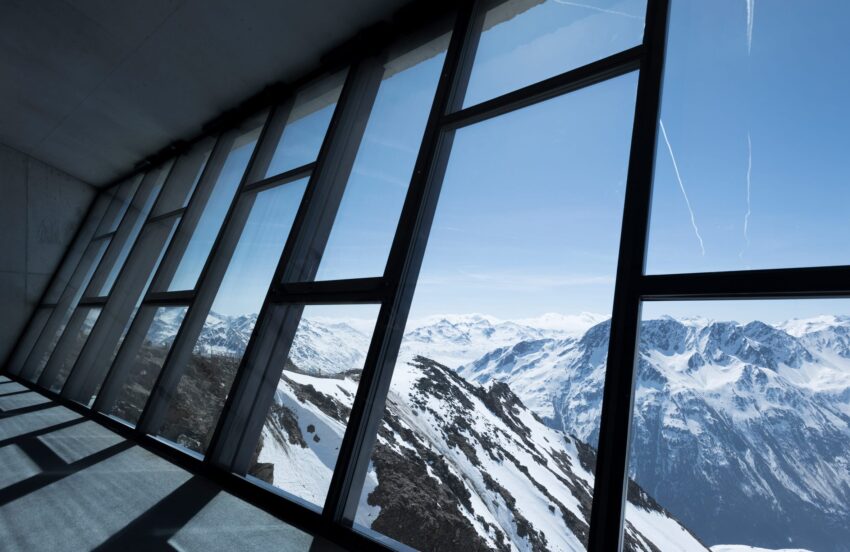 Panoramic view of snow-covered mountains through large glass windows in a modern building.