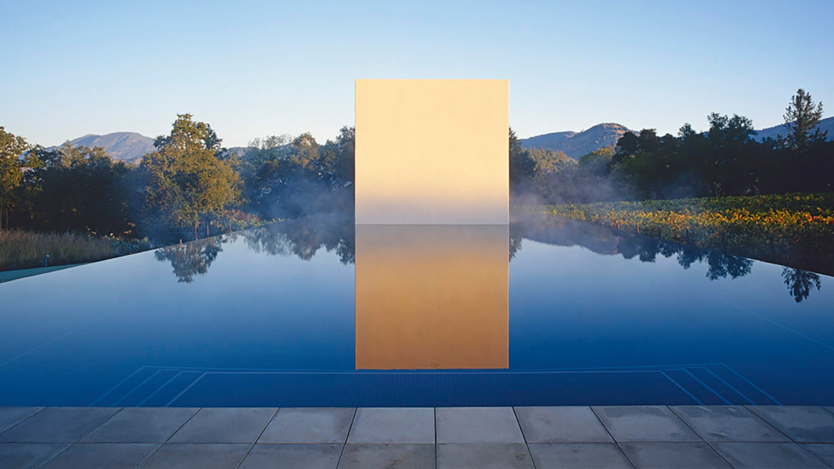 Reflective pool with large golden geometric structure in center, surrounded by mist, trees, and mountains in the background.
