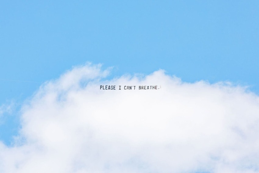 Sky with clouds displaying text "PLEASE I CAN'T BREATHE." written across, set against a clear blue background.