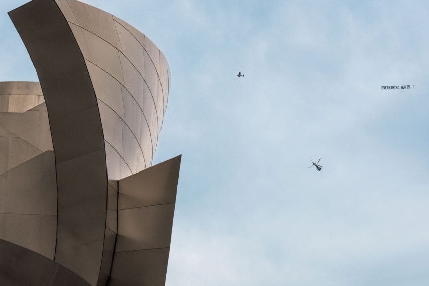 Modern architectural building with curved metal panels and a helicopter flying nearby in a clear sky.